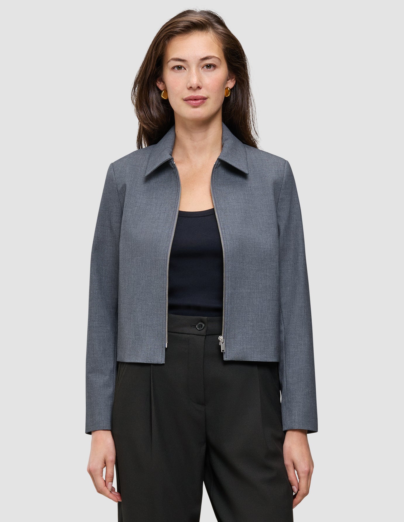 En kvinde har en Essential Short Zip Jacket i mørkegrå melange på over en sort top og bukser.